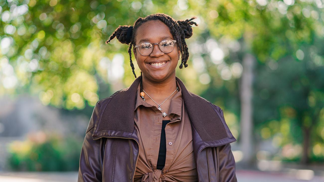 Young woman wearing brown shirt and brown jacket smiling into camera