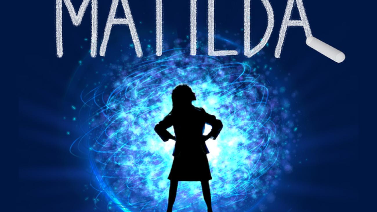 On a deep blue background with a magical round aura in the center, a black silhouette of a small person, wearing a skirt, with their hands on their hips, looks up toward the title of the show [MATILDA] spelled out in chalk above them.