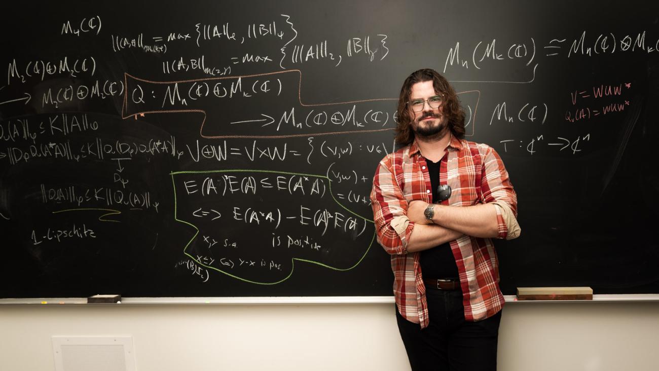 Konrad Aguilar standing in front of blackboard that is covered with mathematical formulas