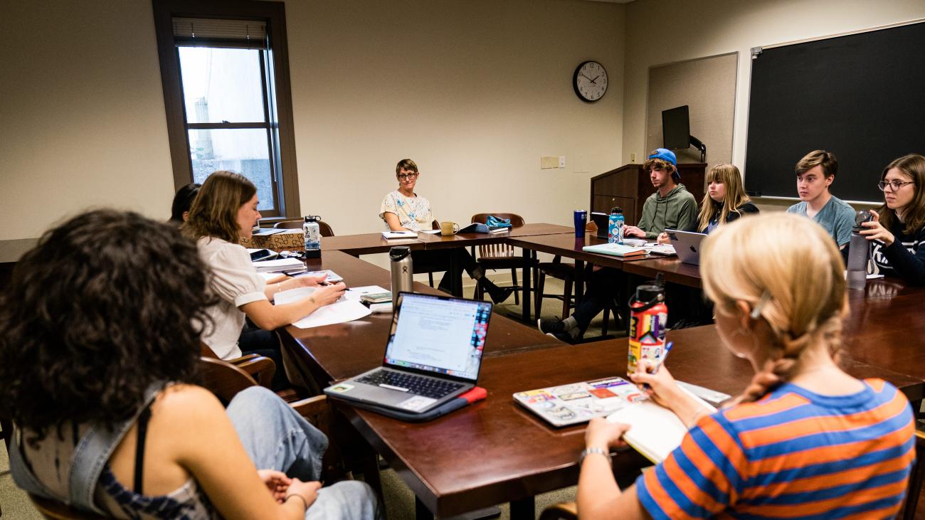 Students sit around table inside classroom.