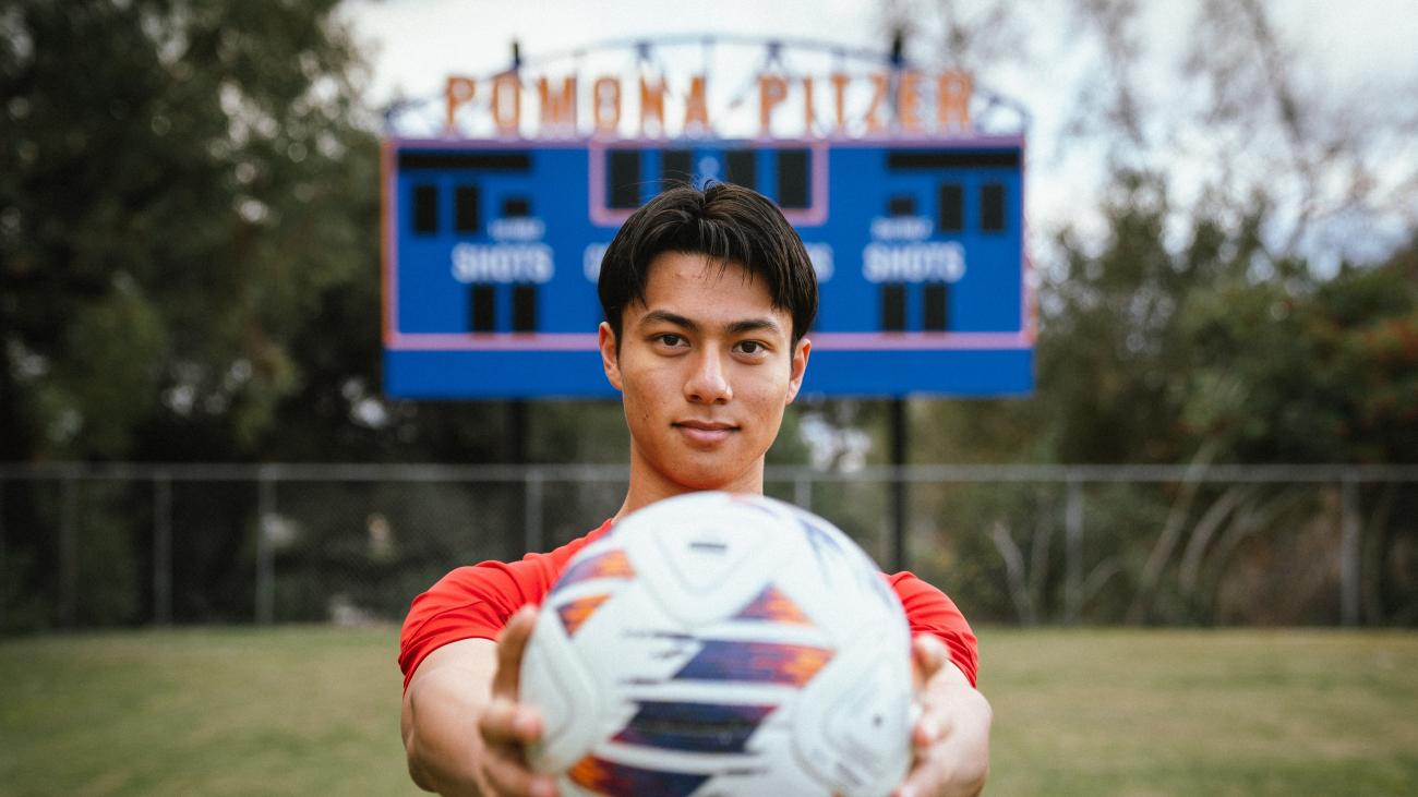 Kyle Lau holds ball in front of Pomona-Pitzer scoreboard