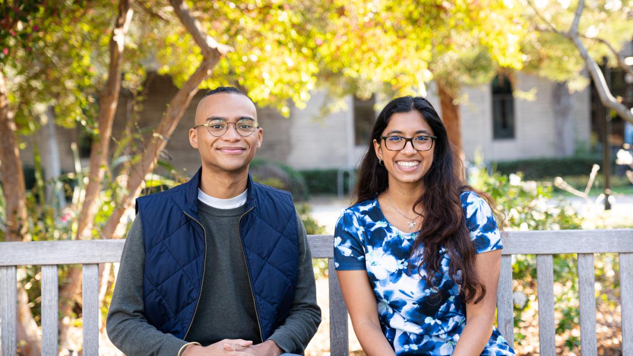 Two students sit on bench smiling