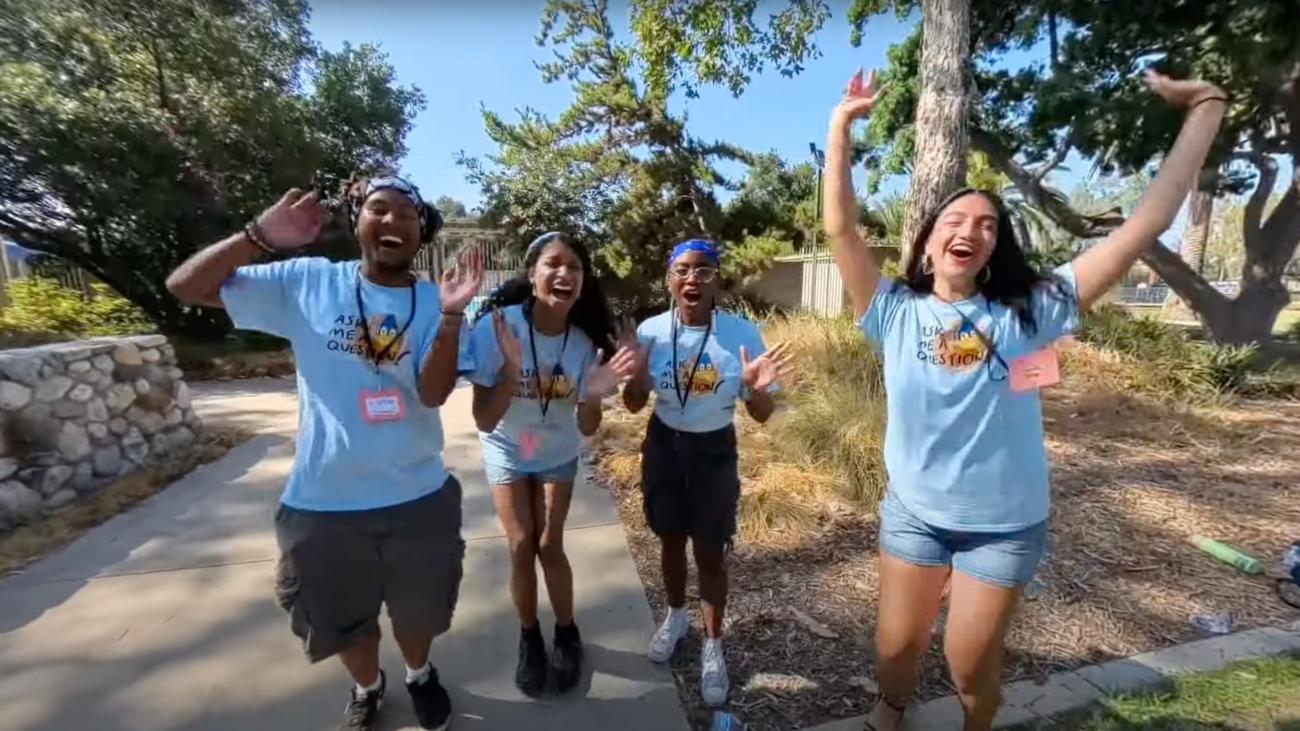 A group of four students excitedly waving to the camera