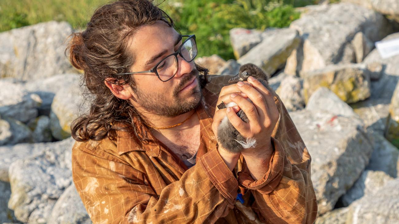 Jacob Ligorria holding seabird chick with rocks in background