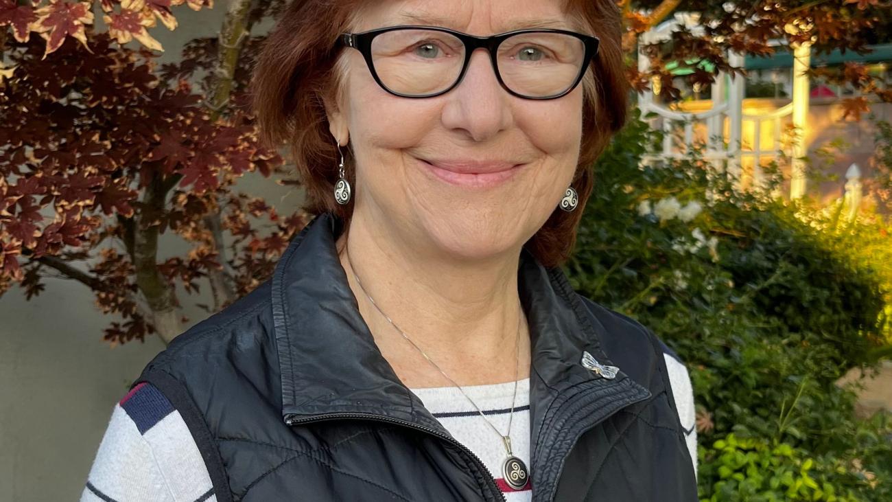 A woman in glasses stands and smiles
