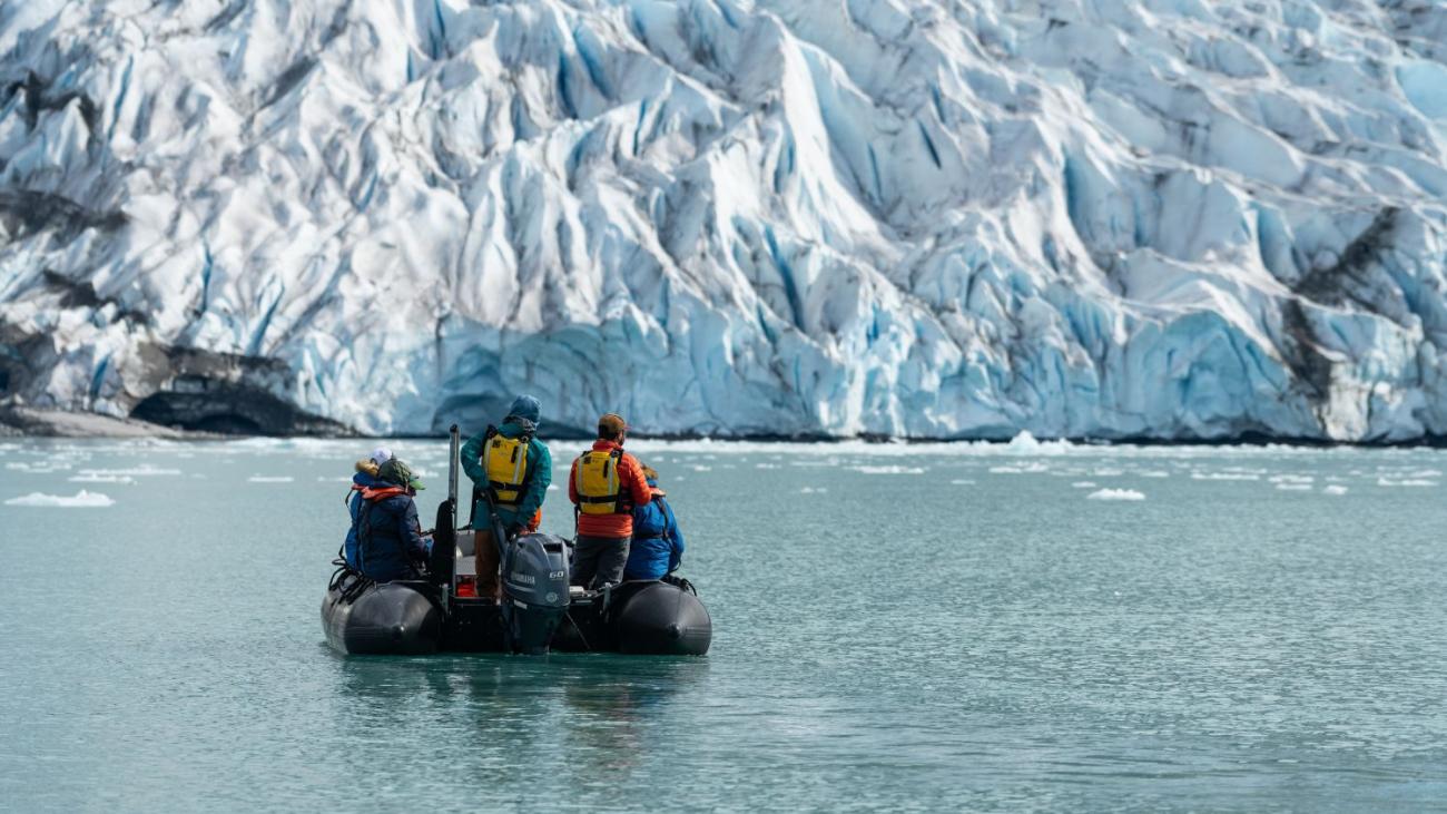 3 people on a small boat gaze at the snowy mountains