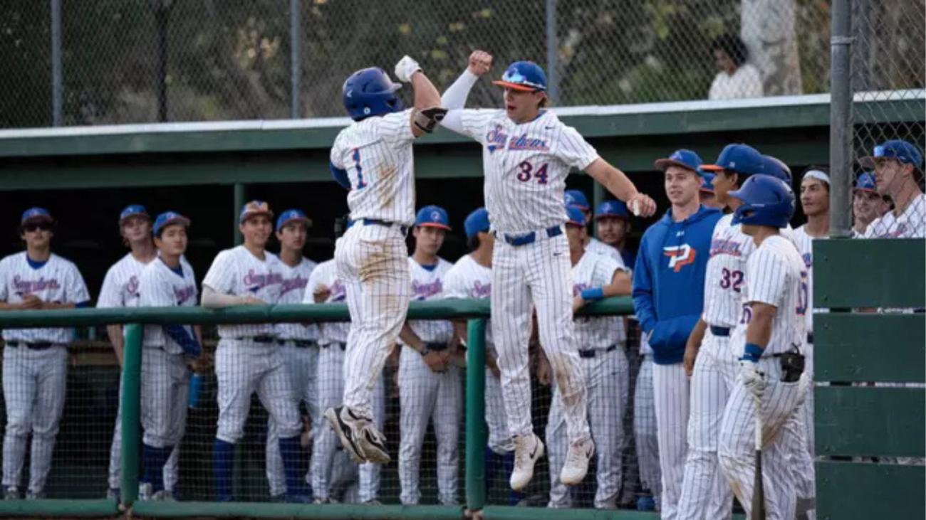 Men's baseball players high-five each other near the dugout