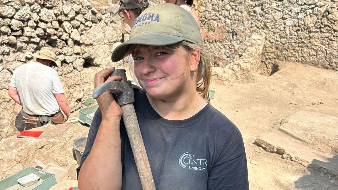 Tristen Leone ’26 at archaeological dig with workers and stone walls in background